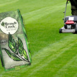 Evolution seed bag superimposed on picture of green lawn being mowed by push mower