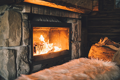 Chimney service Freehold allows for this fire in this fireplace with stone surround. Firewood is in right side of frame and a fuzzy white blanket is in foreground.